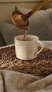a spoon pouring hot liquid into a white cup on a table